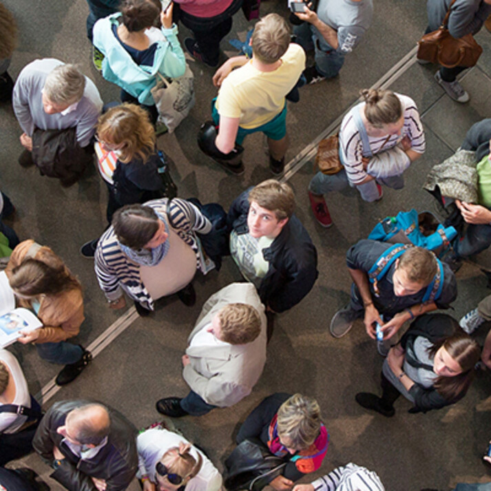 Crowd photographed from above, visitors waiting or moving in an event or exhibition hall.