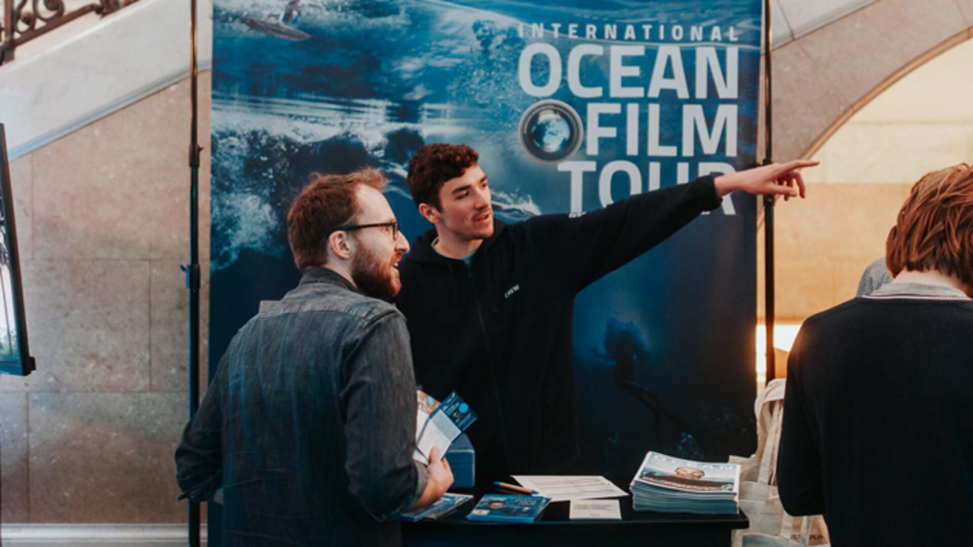 Stand de l’International Ocean Film Tour avec des employés informant les visiteurs et distribuant des brochures.