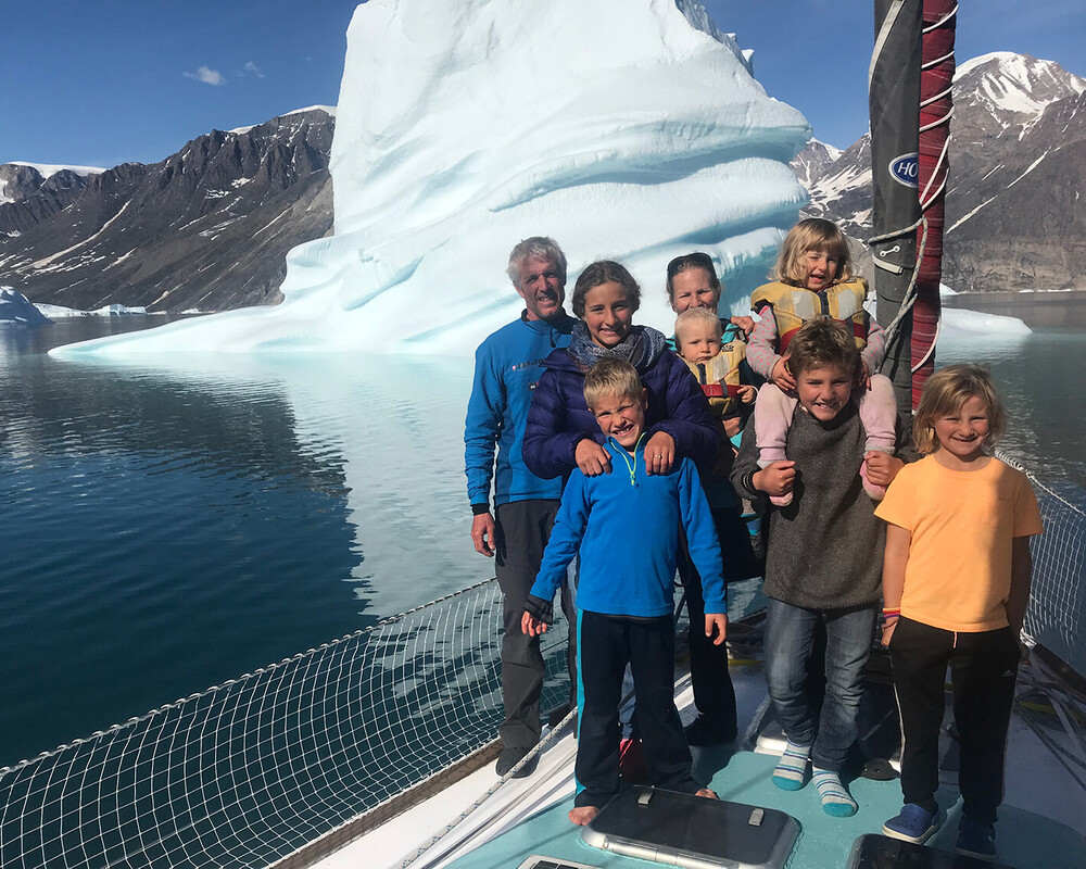 La famille Schw&ouml;rer pose ensemble sur le pont de leur voilier d'exp&eacute;dition TOPtoTOP devant un immense iceberg dans un fjord groenlandais &ndash; parents et six enfants lors d'un voyage de sensibilisation climatique