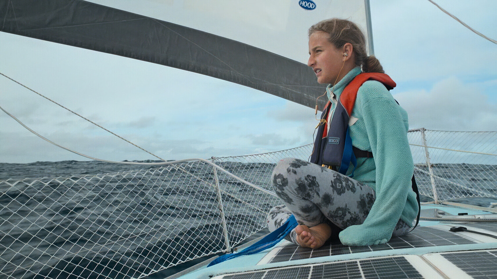 Salina Schw&ouml;rer zit op het dek van de TOPtoTOP expeditie catamaran met een reddingsvest, blootsvoets, uitkijkend over de oceaanhorizon tijdens een offshore zeilpassage